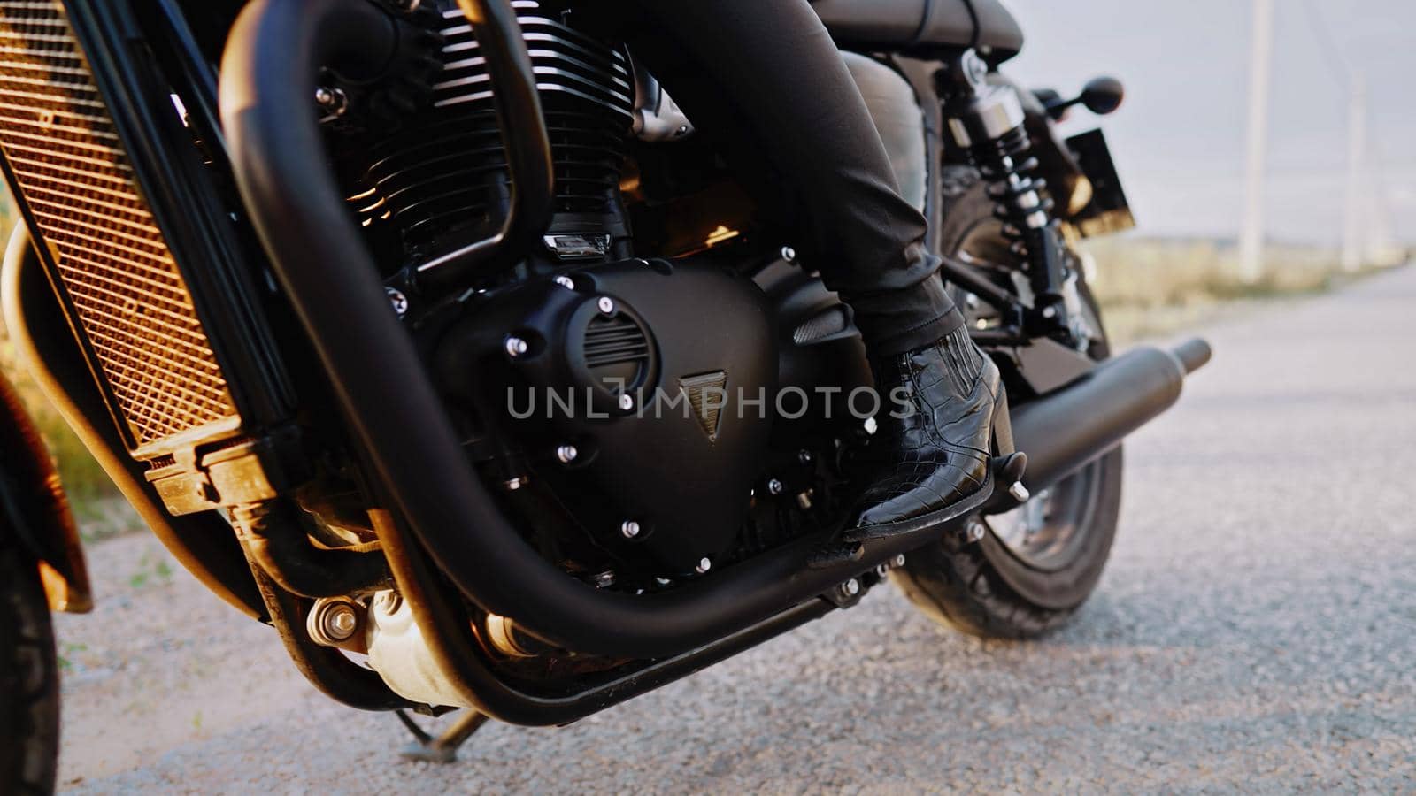 Legs of stylish motorcyclist woman sitting on classic bike. Black retro-styled motorcycle. Details of vintage design of brand-new motorbike. Sun flare, outdoor. High quality photo