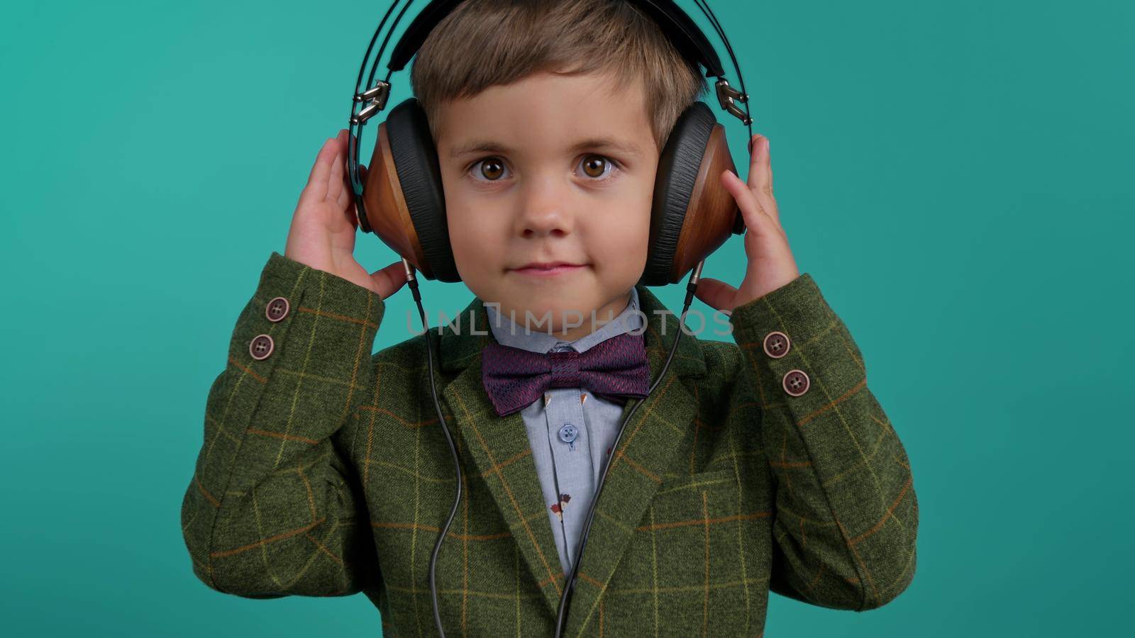 Handsome little toddler boy listening to music with old headphones, child having fun, funny dancing in studio on blue background. Dance, radio, analog concept. High quality photo