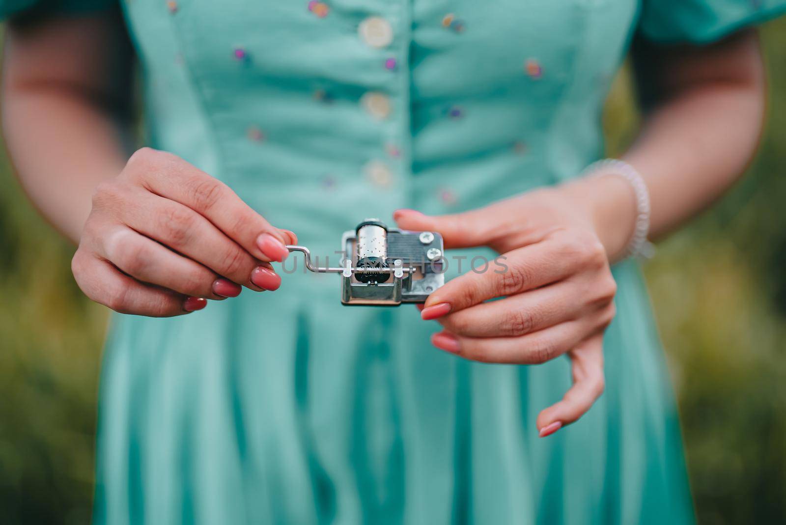Female hands rotating gears of old music box mechanism. Lady turning lever of retro small metallic carillon. Woman in vintage dress listening to music which playing. High quality photo