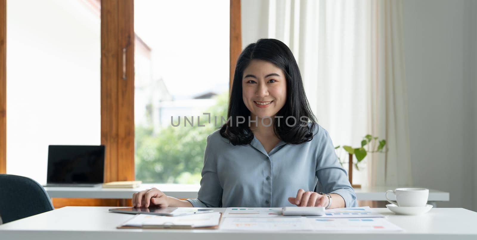 Charming asian businesswoman sitting working on laptop for paperwork in office by nateemee