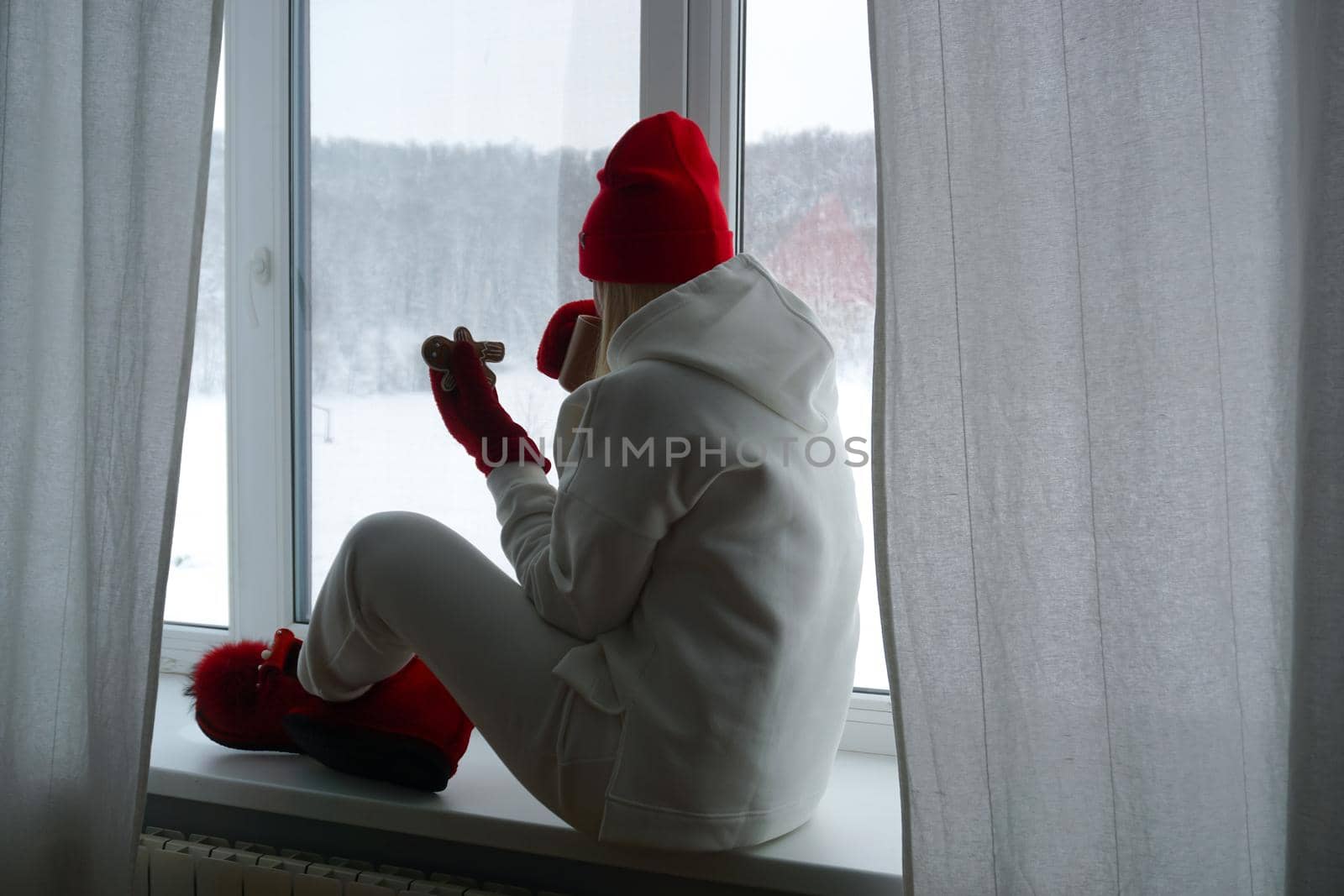 A woman in a white suit sits on the windowsill and looks out the winter window by Spirina