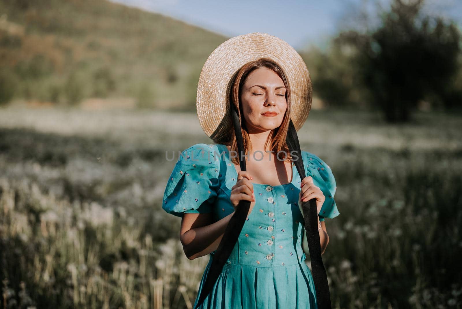 Young stylish woman in vintage dress and straw hat alone on nature in countryside. Carefree lifestyle, romantic girl. Retro fashionista like from novel. High quality photo