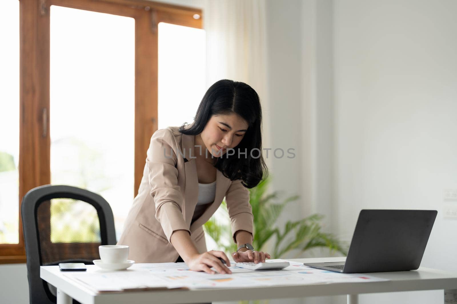 Woman with paperwork using calculator and laptop computer working at home office.