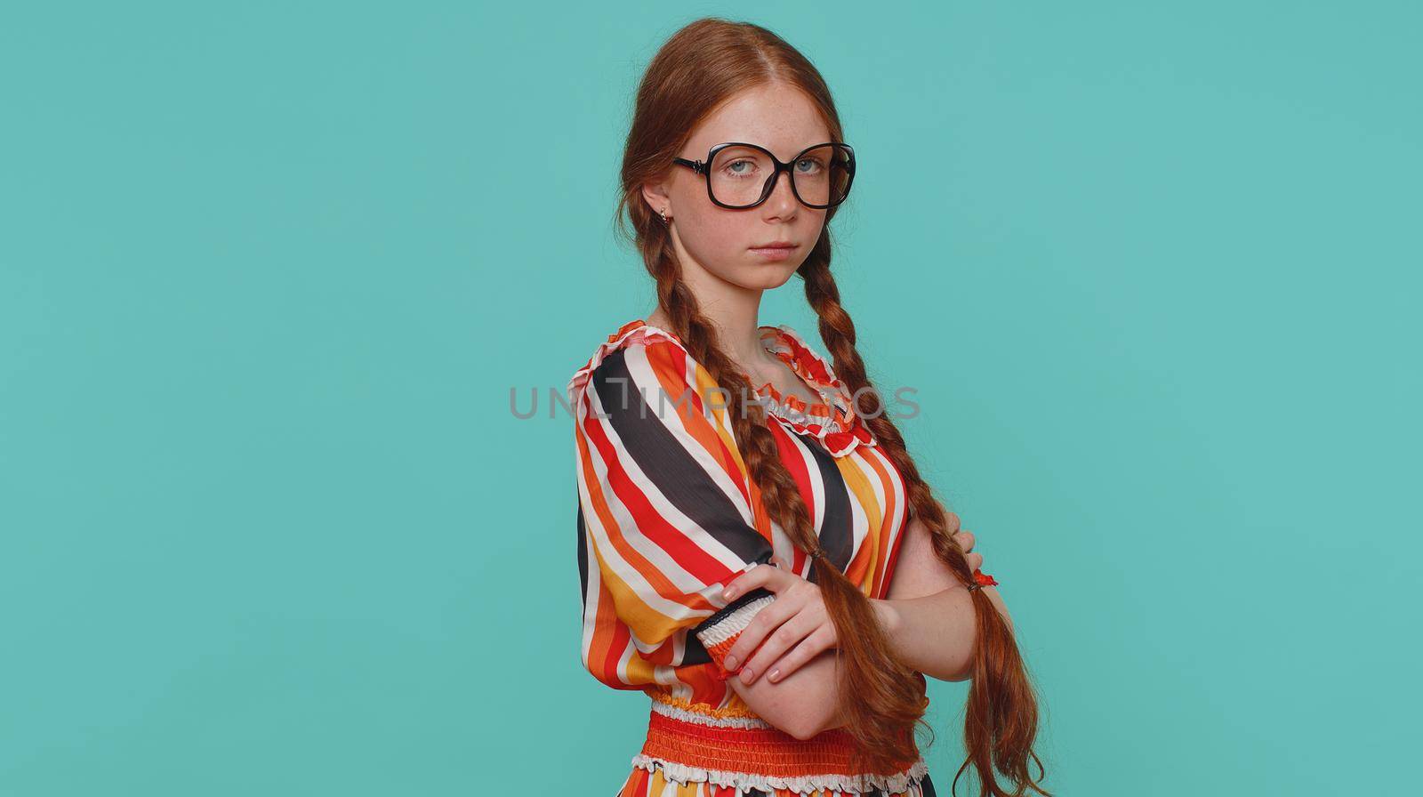 Offended redhead girl having misunderstanding, frustrated after quarrel, ignores and does not want to communicate, talk. Young angry teenager ginger child kid indoor isolated on blue studio background