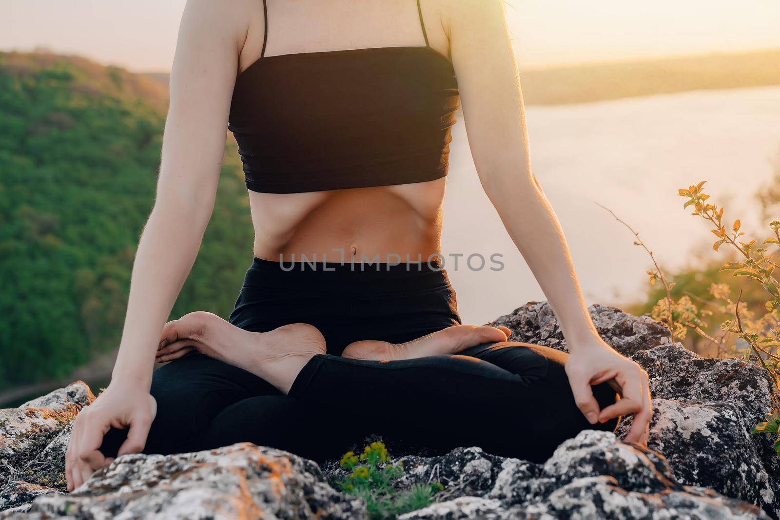 Woman doing yoga belly exercise - Kapalabhati yogic breathing technique. Yogi does uddiyana bandha, sitting in lotus pose on high cliff above water outdoors.Lady breathing, meditating. quality photo