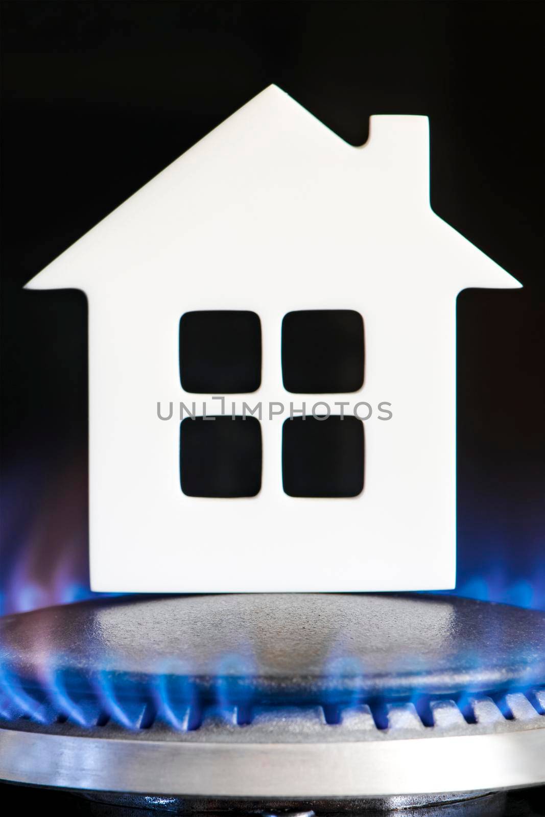 Heating season. The beginning of the heating season on natural gas. Concept, model of a house stands near the flame of a gas boiler on a black background. Home heating cost