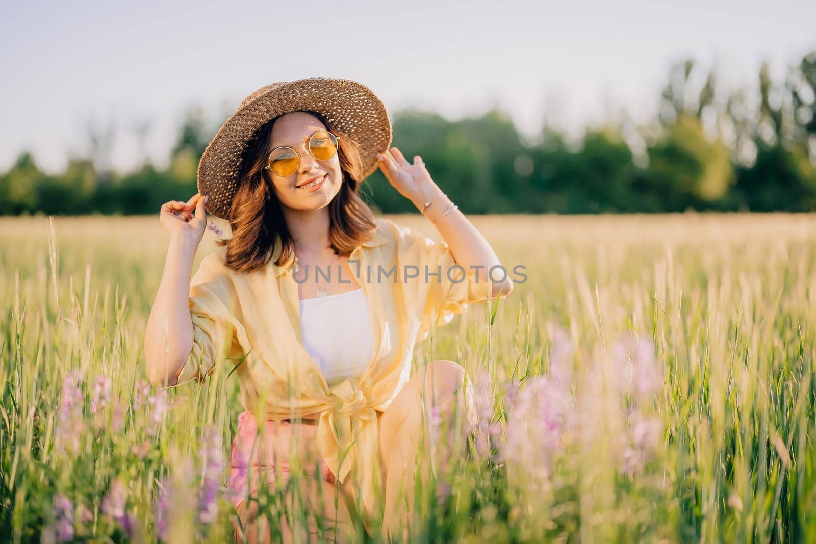 Portrait of happy woman in straw hat in fresh green wheat field. Grass background. Amazing nature, farmland, growing cereal plants. Stylish lady with eyewear. High quality photo
