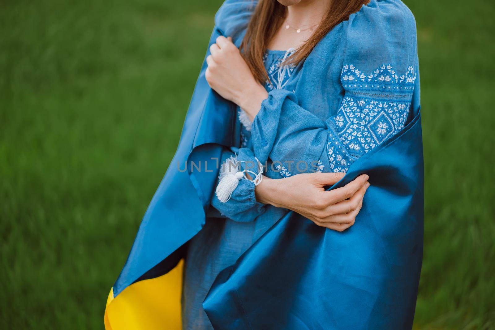 Smiling ukrainian woman with national flag on green field background. Young lady in blue embroidery vyshyvanka. Ukraine, independence, freedom, patriot symbol, victory in war. High quality photo