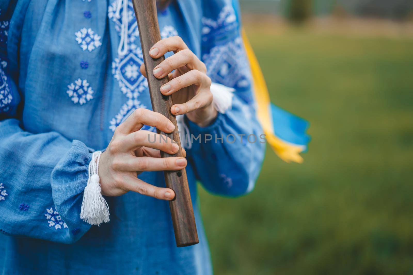 Woman playing woodwind wooden flute - ukrainian sopilka outdoors. Folk music, culture concept. Musical instrument. Lady in traditional embroidered shirt - blue vyshyvanka. High quality photo