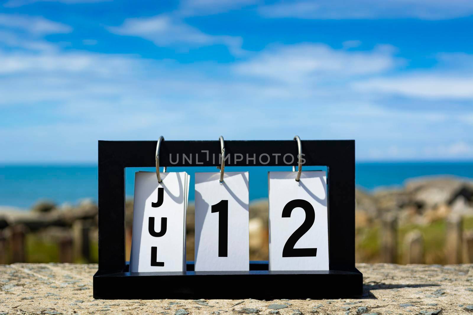 Jul 12 calendar date text on wooden frame with blurred background of ocean. Calendar date concept.
