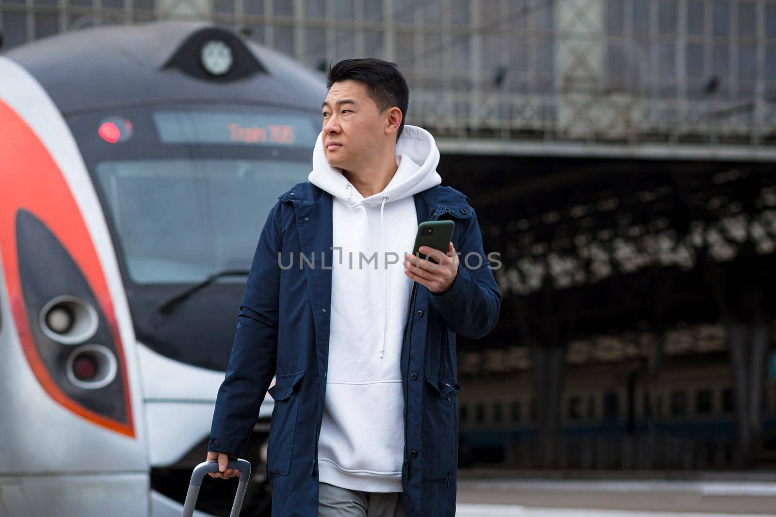 Male Asian businessman, at the train station, buys train tickets online, uses a mobile phone and an application, the tourist returns home from a business trip