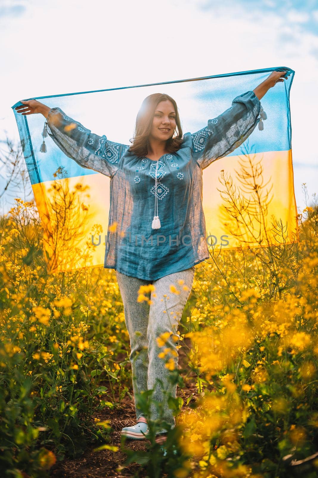 Pretty ukrainian patriot woman with national flag in canola yellow field. Ukraine unbreakable, peace, independence, freedom, victory in war. High quality photo