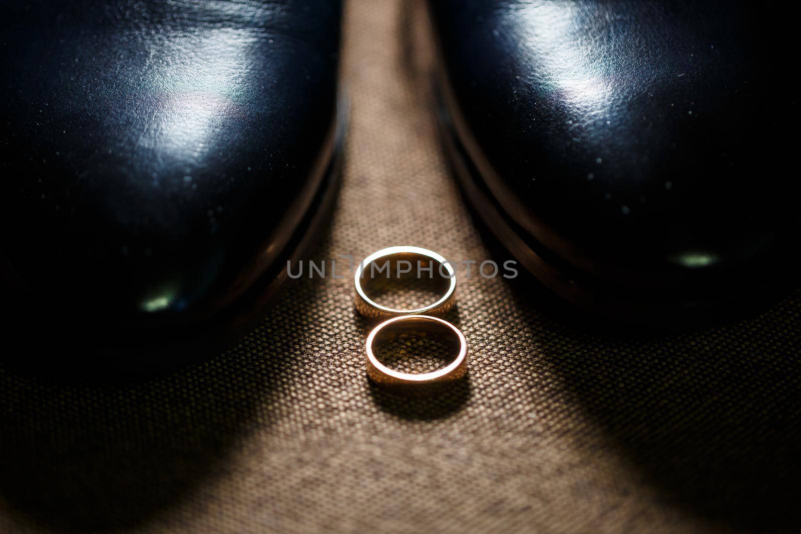 Gold wedding rings of the newlyweds lie next to men's shoes for the groom