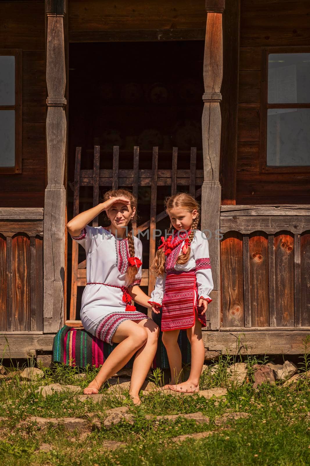 mother and daughter in Ukrainian folk dresses are sitting near the house by zokov