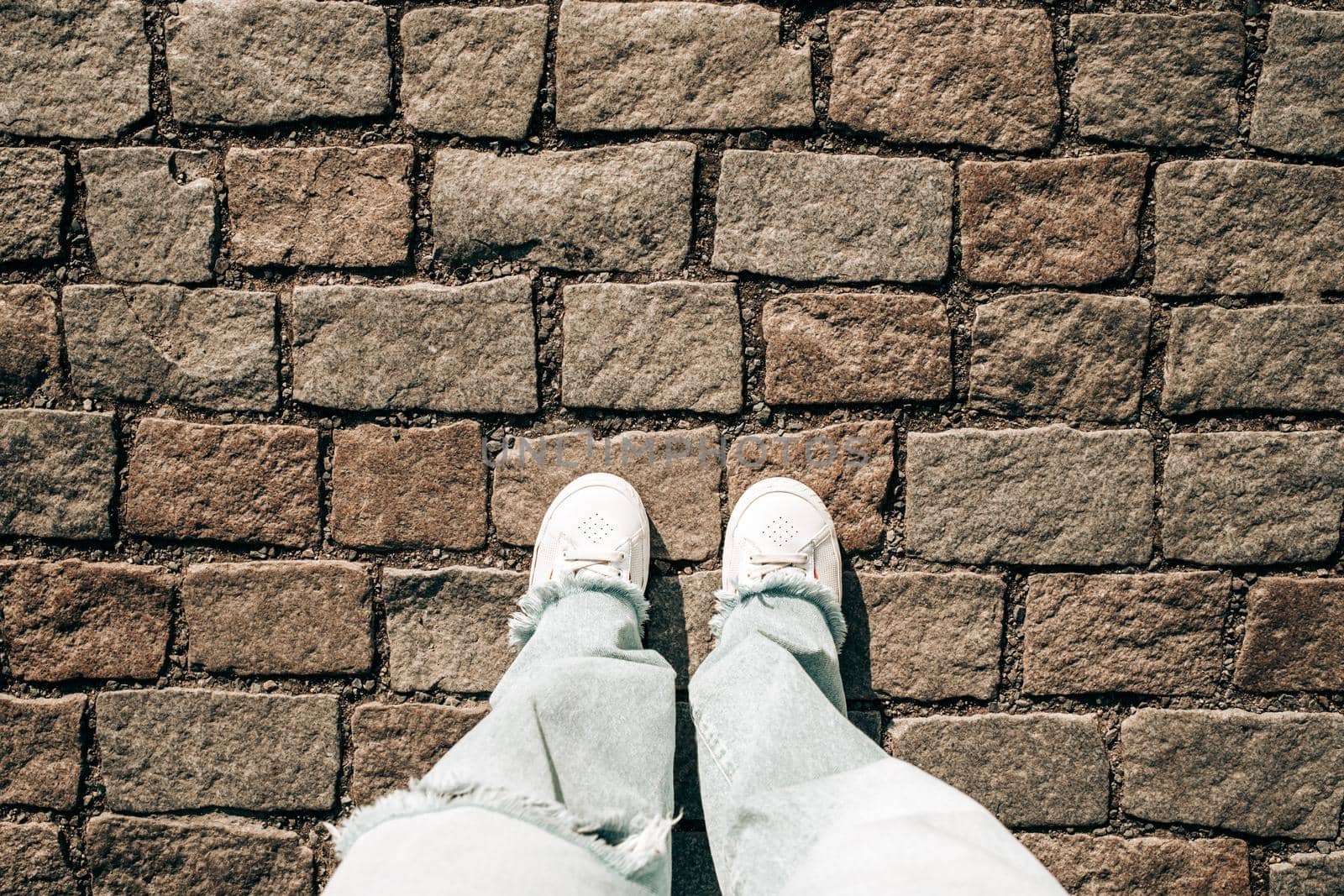 Female legs in jeans and white sneakers on paving stones. Teenage feet top view. Prague street, old city. High quality photo