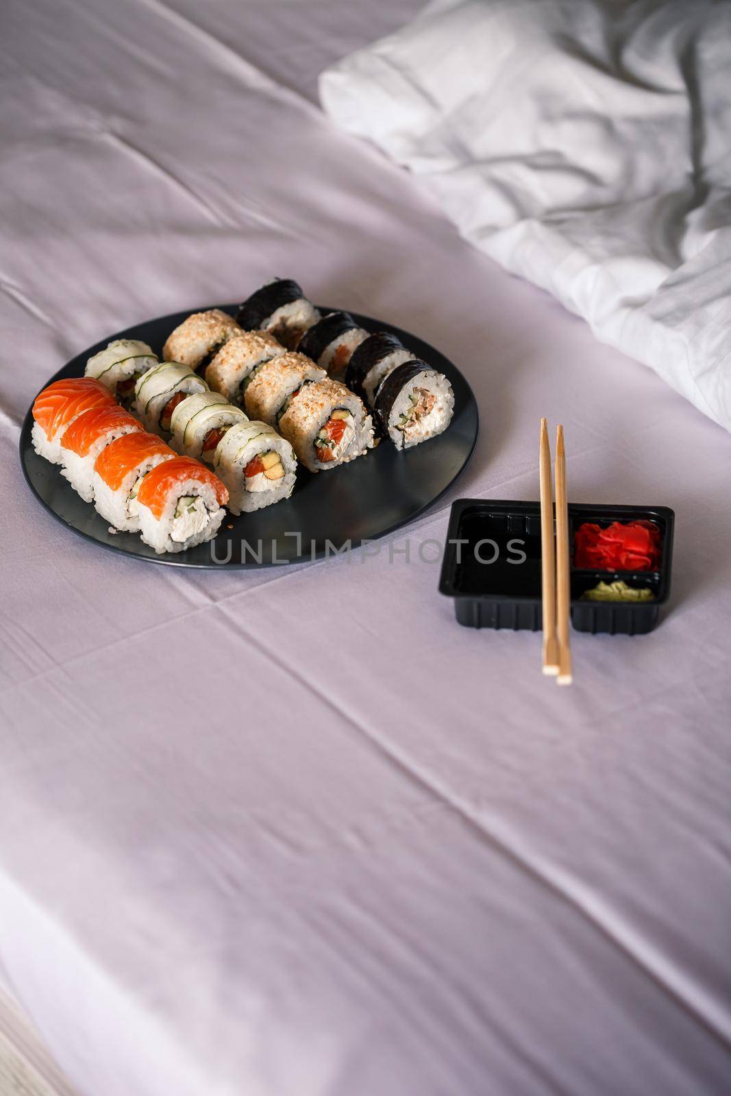 A plate with a sushi set stands on a white bedspread, rolls for a romantic dinner. Traditional japanese food by Dmitrytph