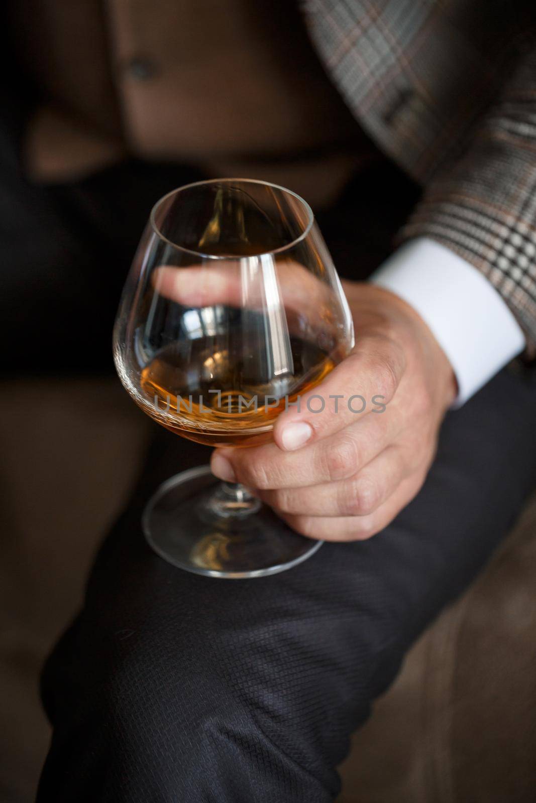 A man businessman holds a glass with alcohol in his hand. Dressed in a jacket and shirt. Rest after a working day. Selective focus