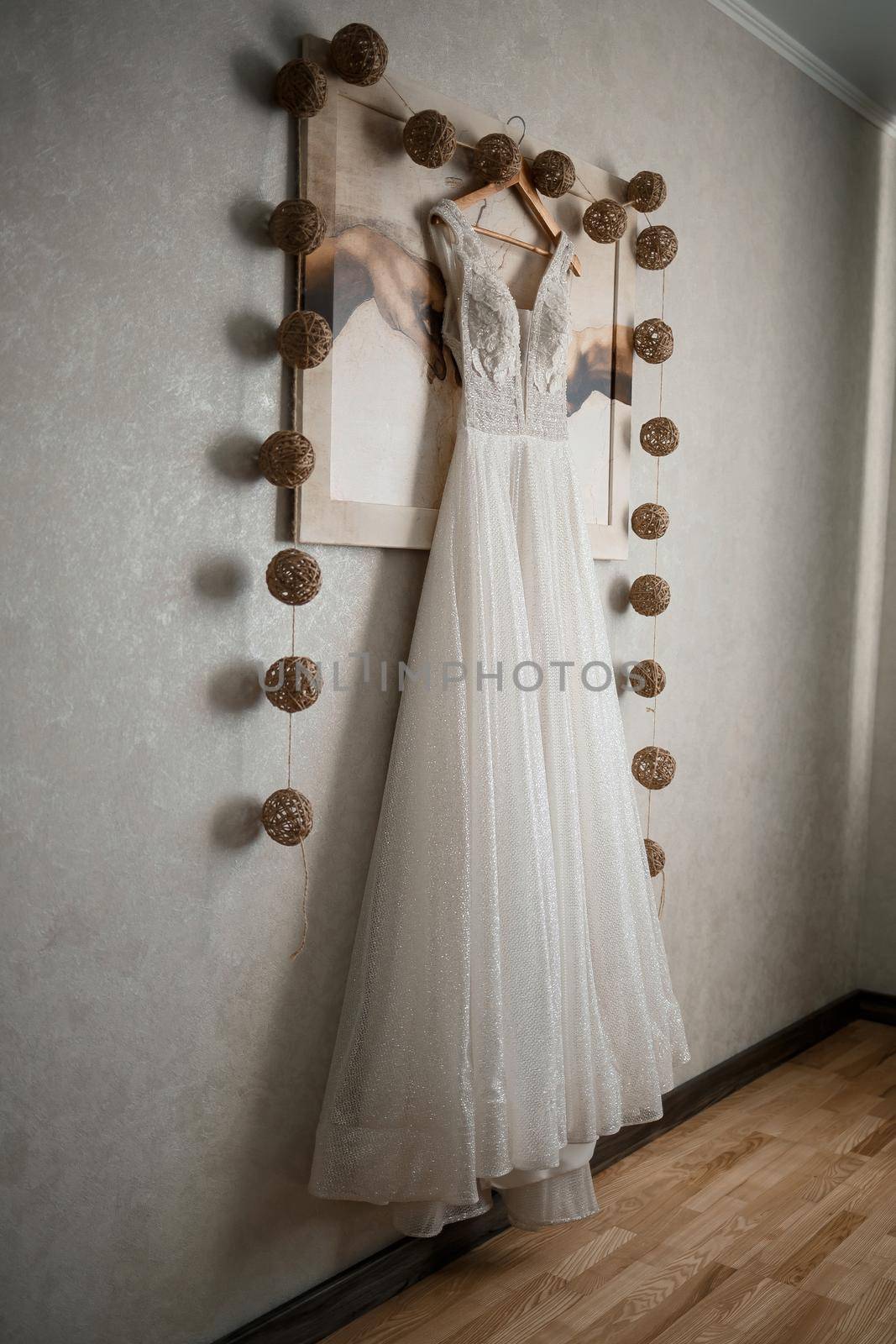 Ivory lace wedding long dress hanging on a wooden hanger by Dmitrytph