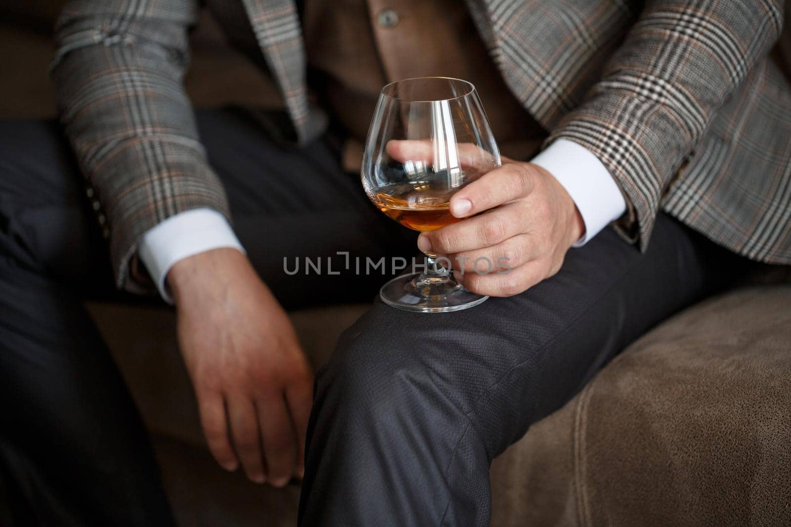 A man businessman holds a glass with alcohol in his hand. Dressed in a jacket and shirt. Rest after a working day