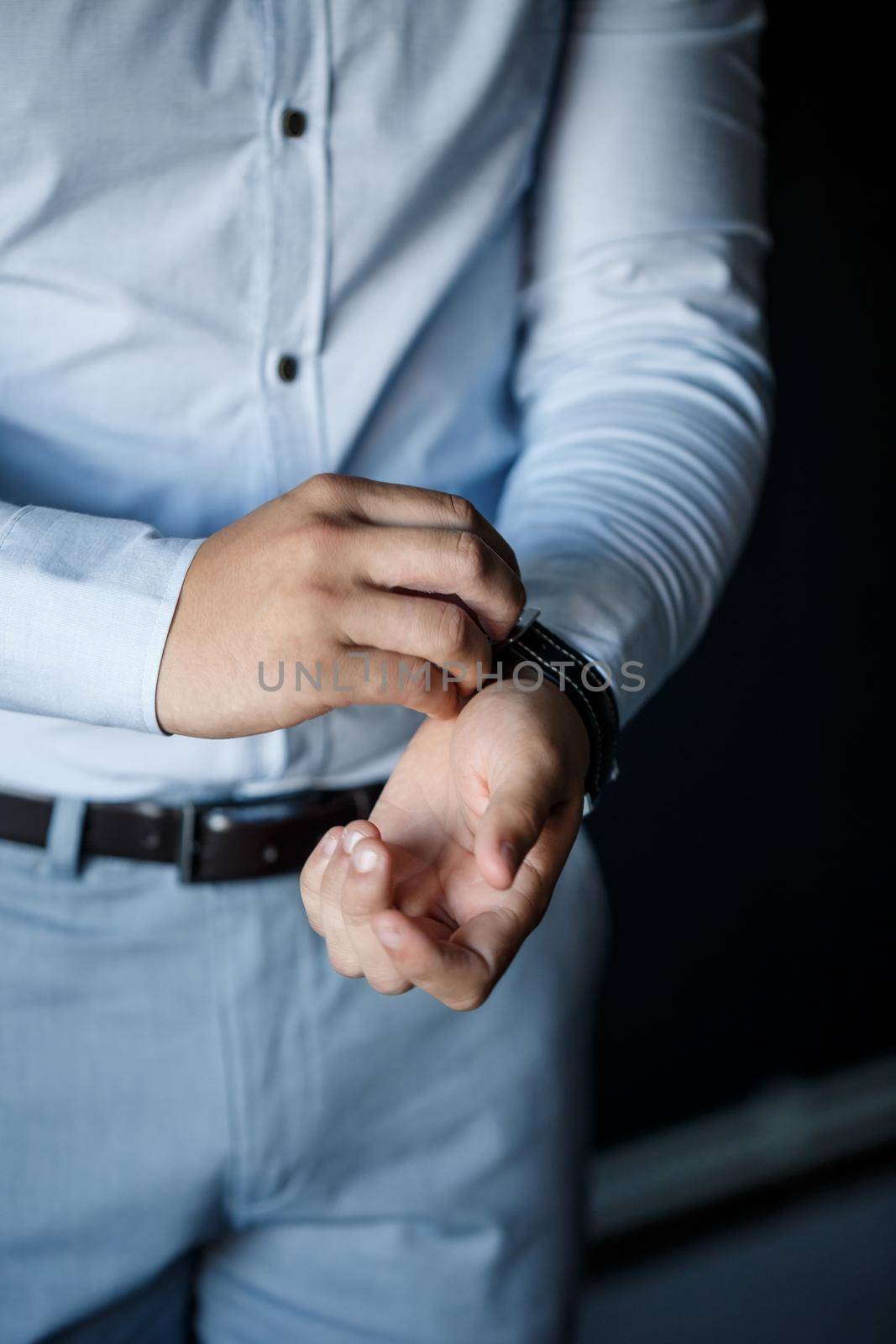 A man elegant businessman buttons a watch on his hand he is dressed in a white dress shirt