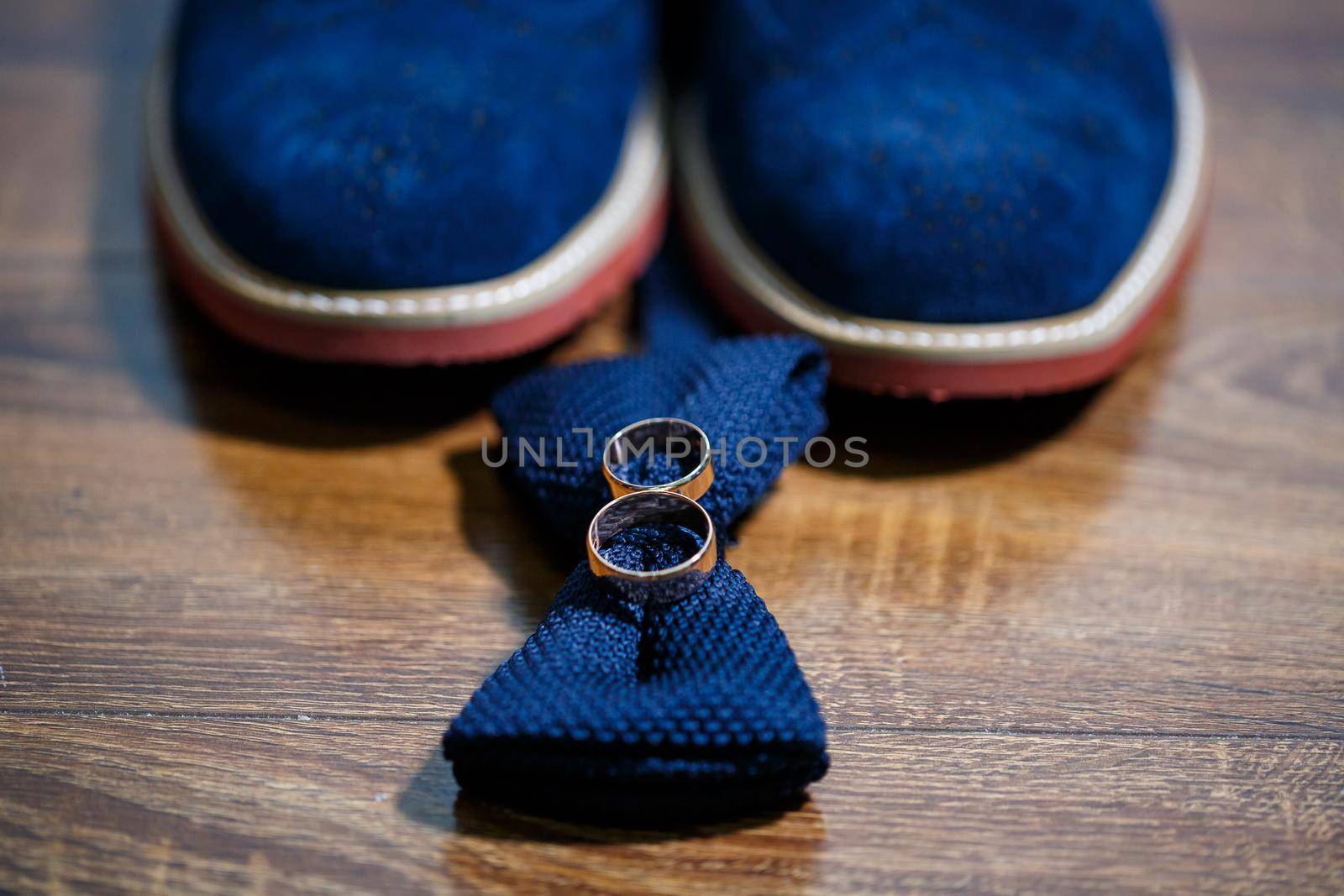 Gold wedding rings of the newlyweds lie next to men's shoes for the groom