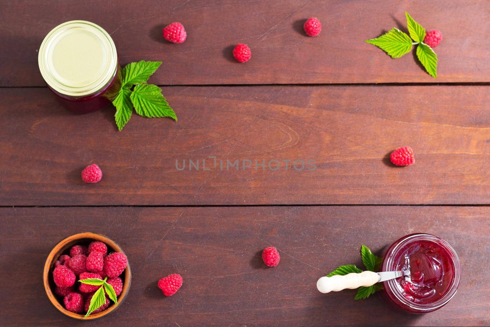 fresh raspberry jam in a glass jar on a wooden table, next to fresh raspberries. concept of homemade jam, preserves for winter, selective focus and copy space