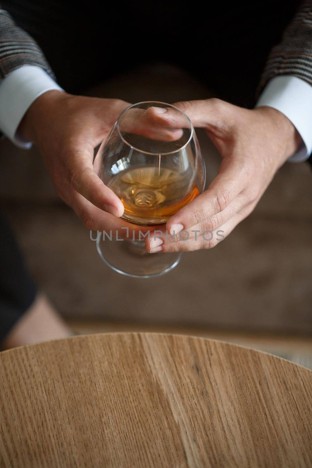 A man businessman holds a glass with alcohol in his hand. Dressed in a jacket and shirt. Rest after a working day