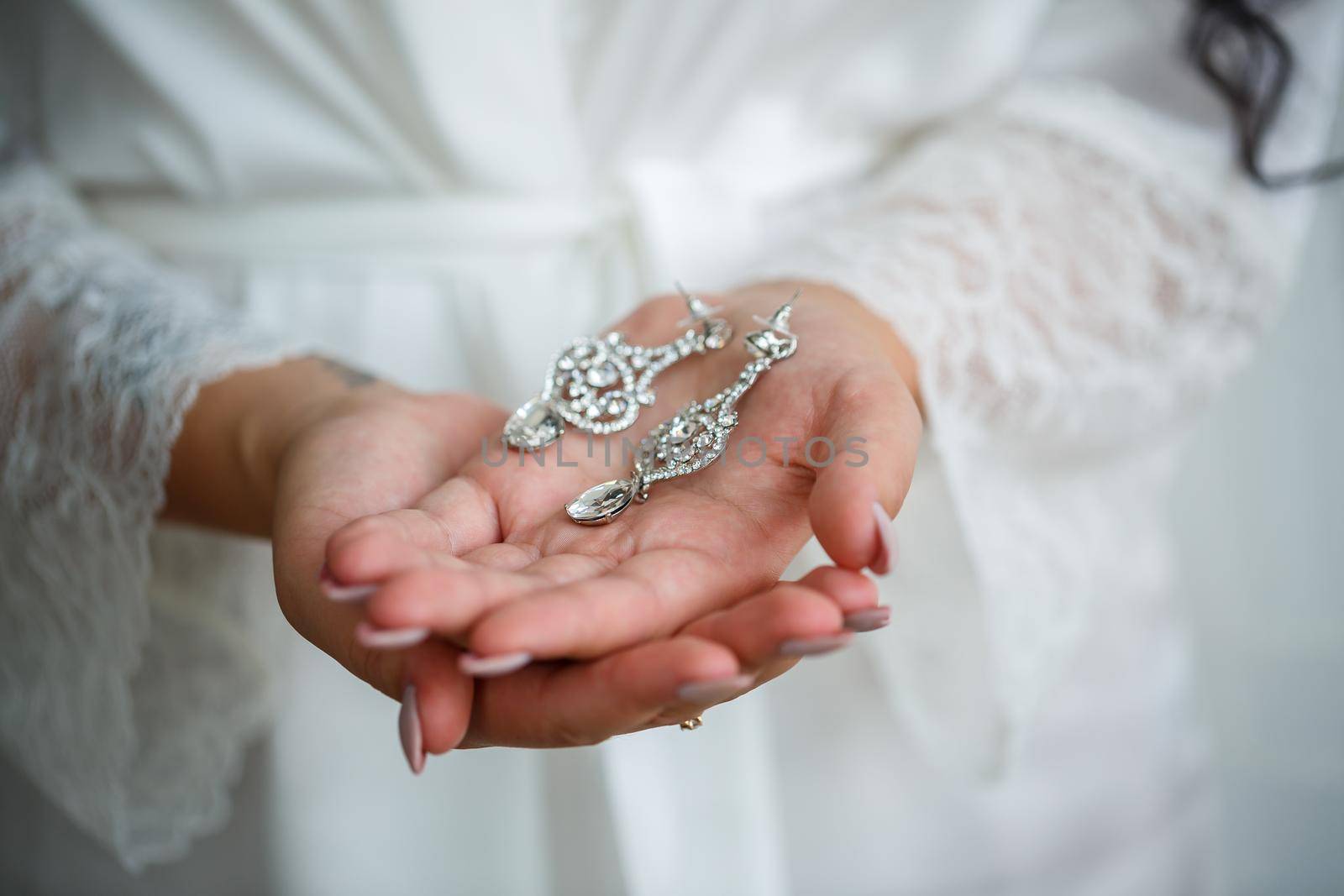 The bride holds earrings in her hand on her wedding day. Jewelry for a holiday for the newlyweds