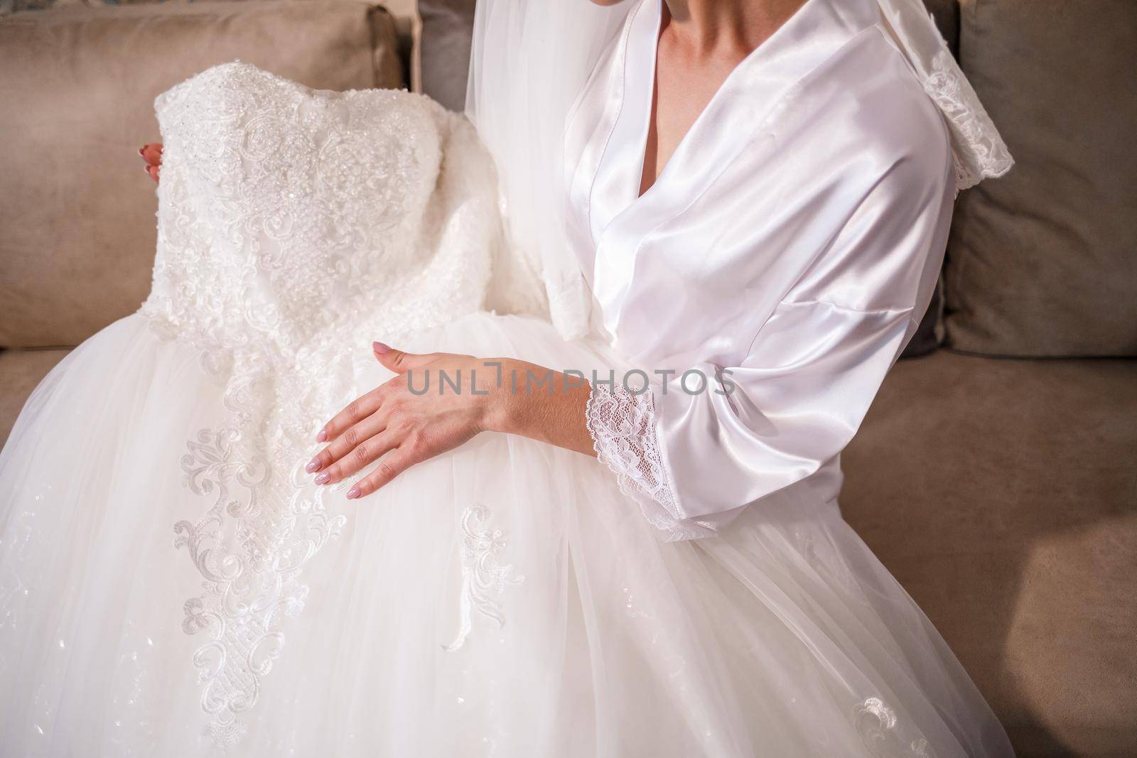 The bride holds a white dress in her hands on the wedding day.