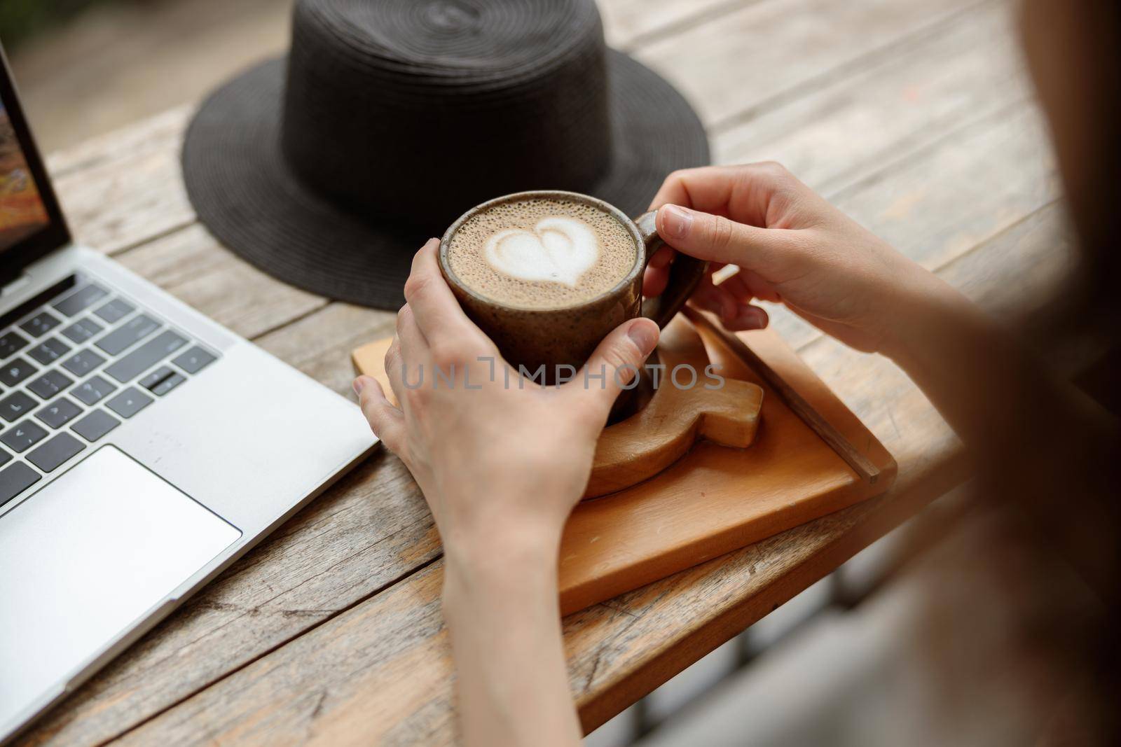 Female hands holding cup of hot drink while working with laptop by Yaroslav_astakhov