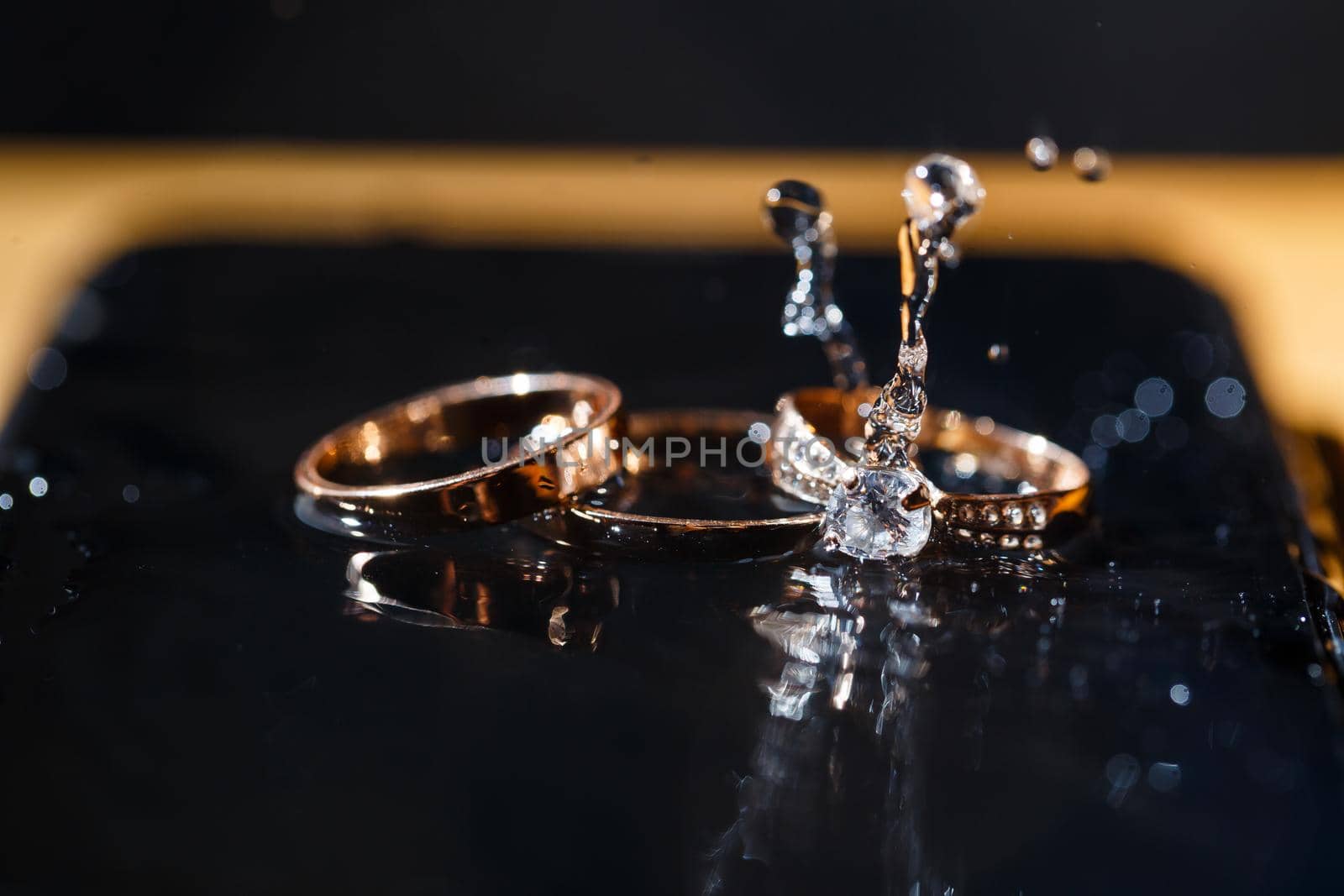 gold wedding rings for newlyweds on a wedding day on a black background with water drops. Jewelry