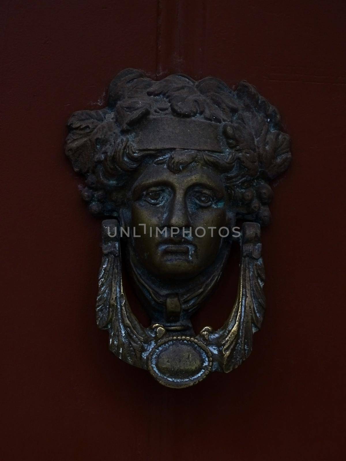 Door knocker in the form of the head of Dionysus on a burgundy wooden door close up