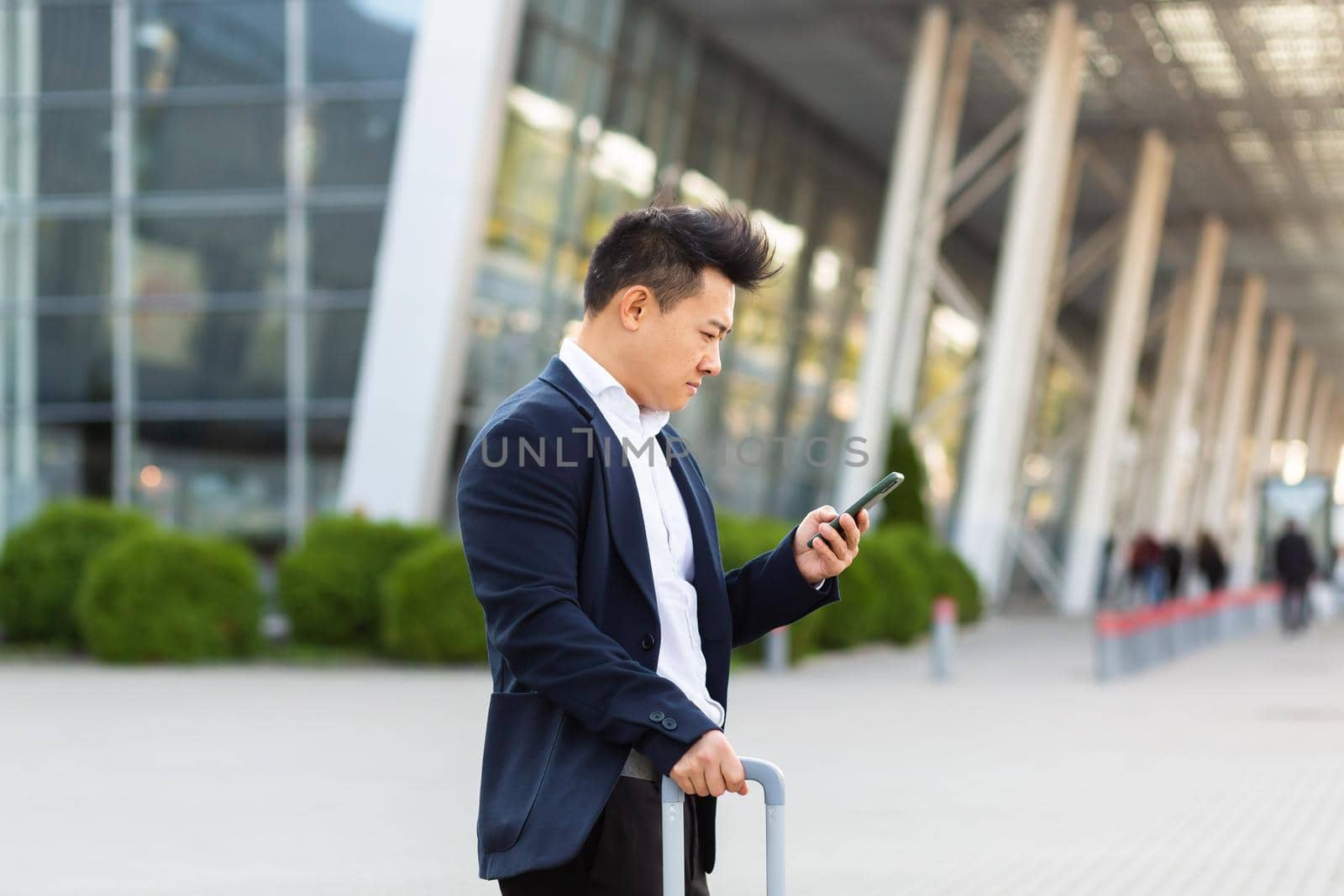 Businessman trying to call a taxi using an app and a mobile phone, asian man at the train station with a big suitcase