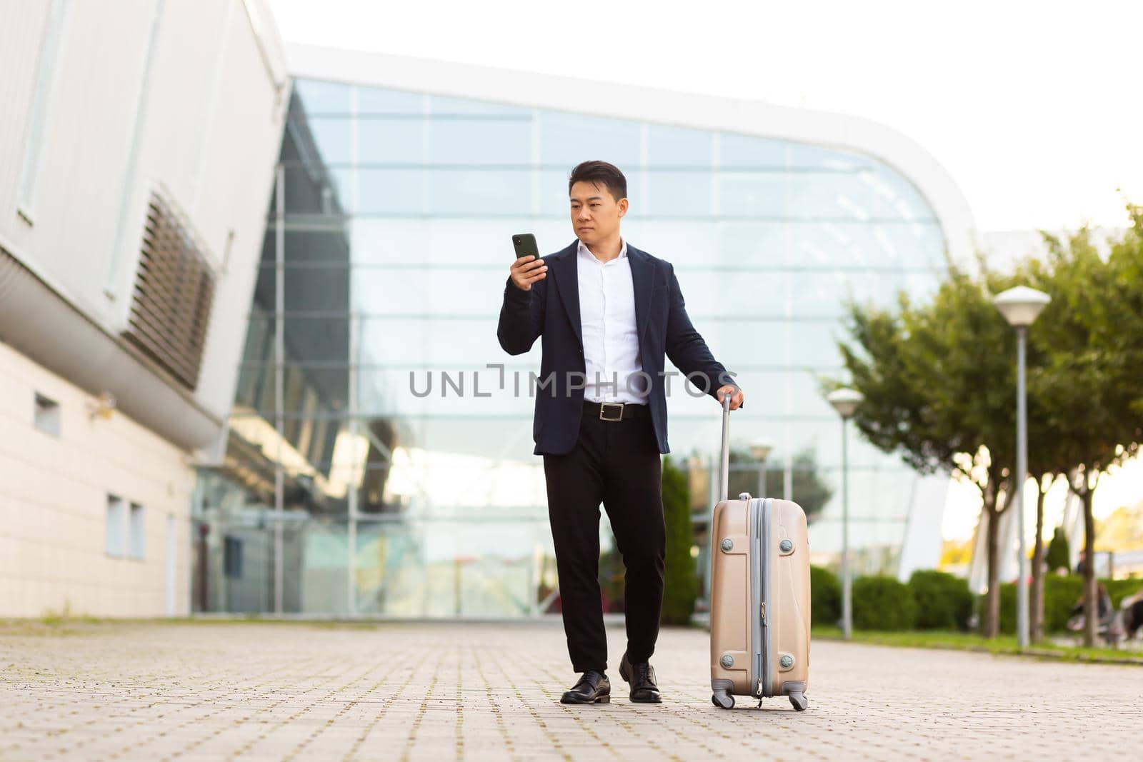 Businessman trying to call a taxi using an app and a mobile phone, asian man at the train station with a big suitcase