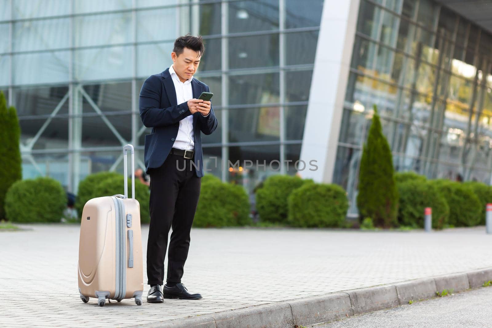 Businessman trying to call a taxi using an app and a mobile phone, asian man at the train station with a big suitcase