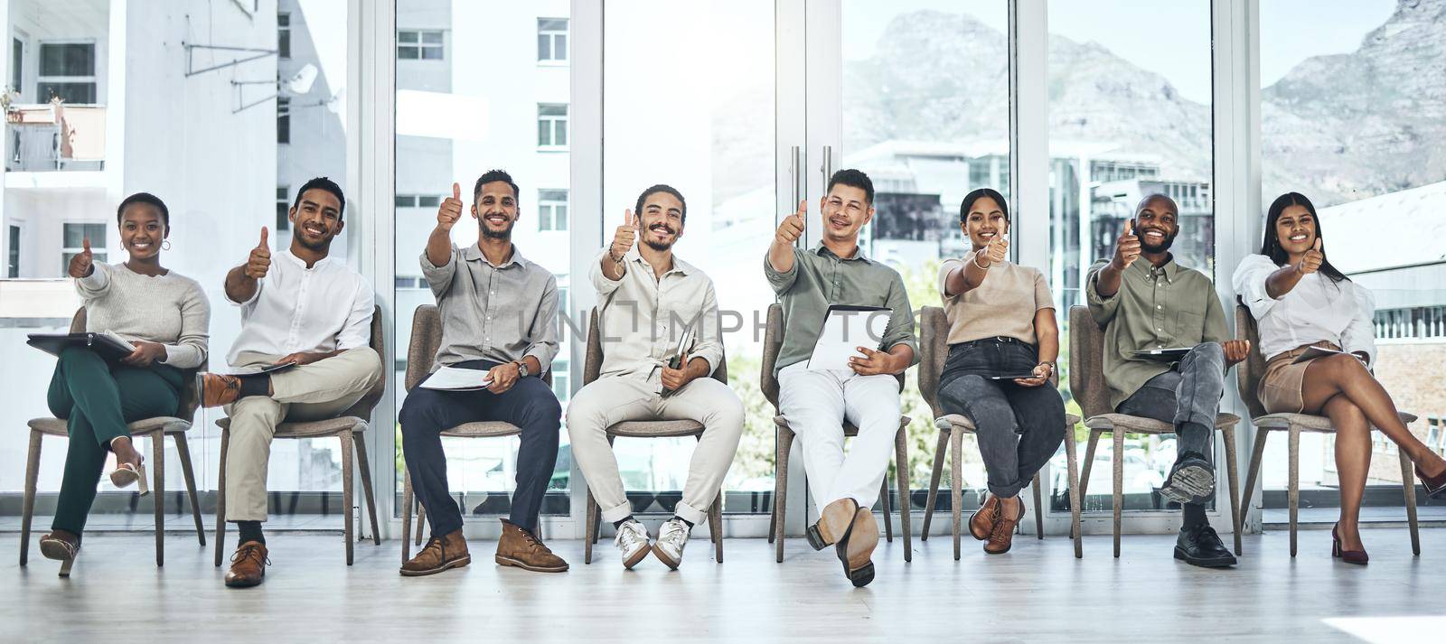 Do you love your job. a group of people showing thumbs up in a modern office. by YuriArcurs