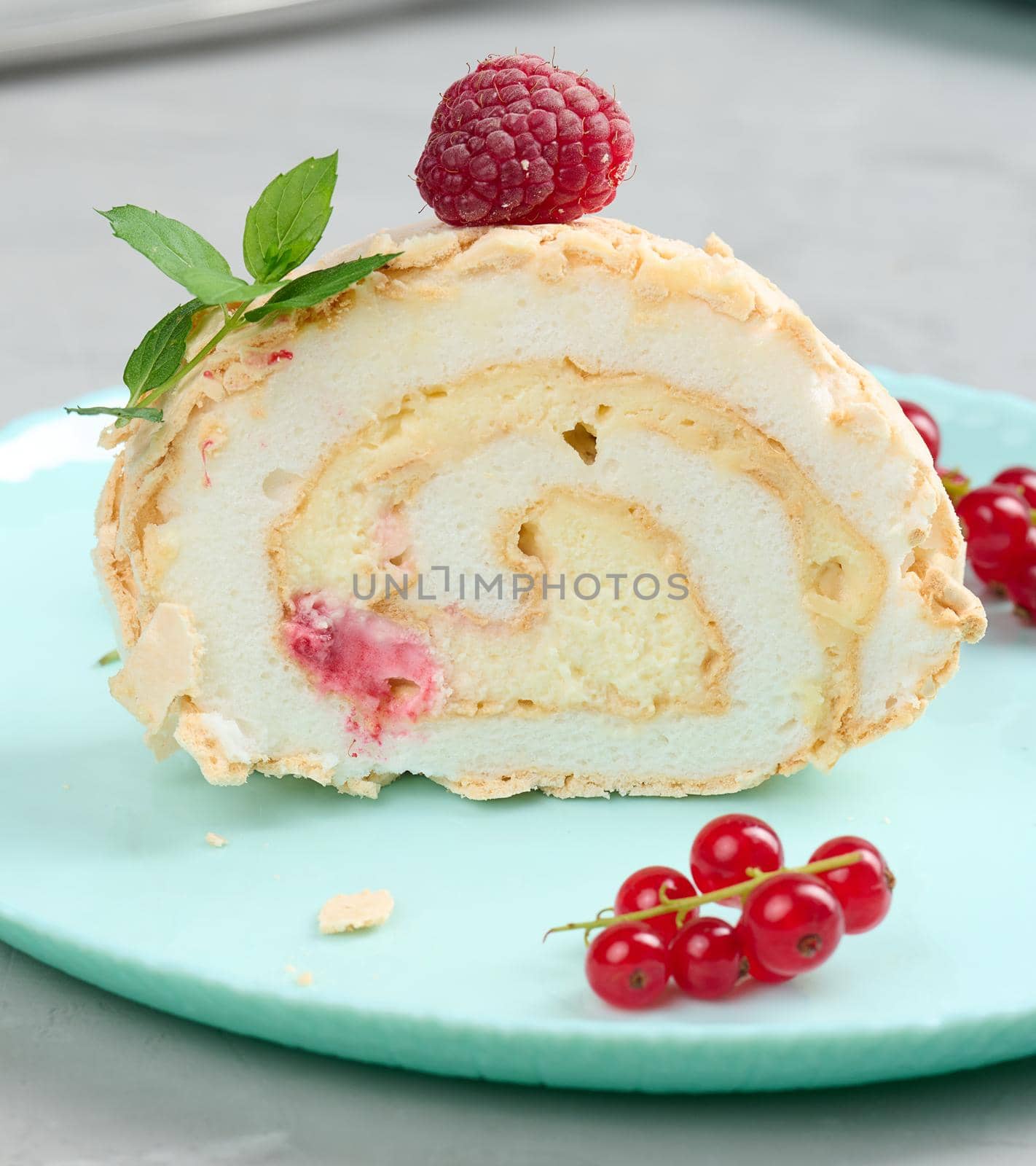 Baked meringue roll with red berries on a round plate, white background