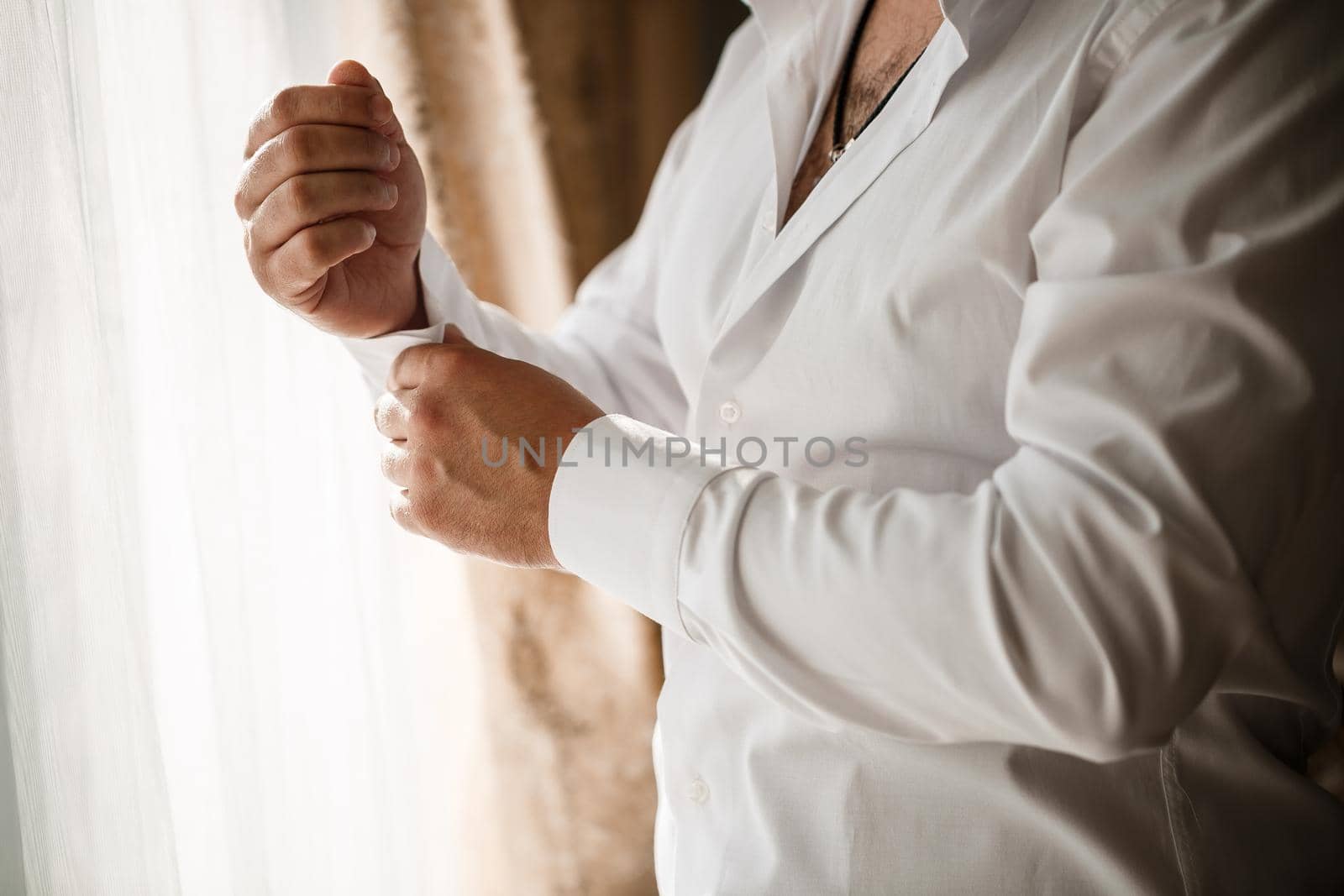 Man businessman buttoning a button on the sleeve of a white dress shirt