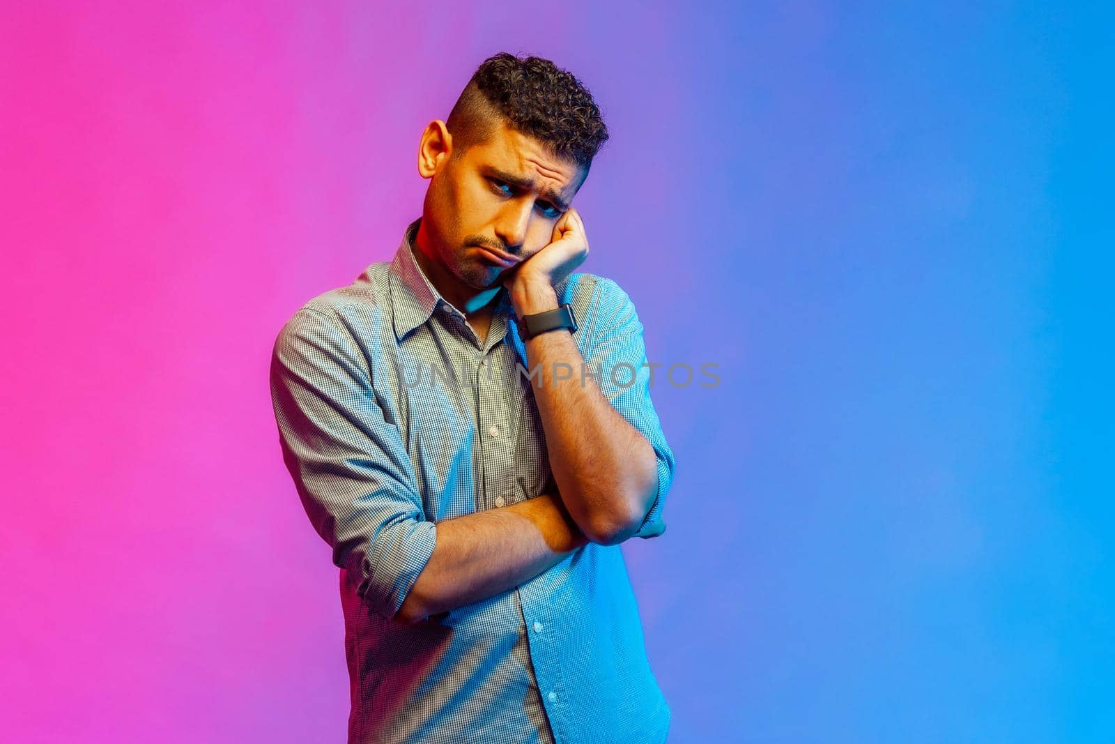 Portrait of depressed man in shirt looking at camera with unhappy sad expression, tired of being lonely, feels bored. Indoor studio shot isolated on colorful neon light background.