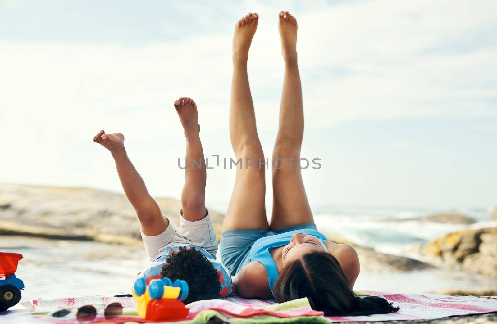 I wish you would always stay young. a mother and her son playing putting their legs in the air at the beach. by YuriArcurs