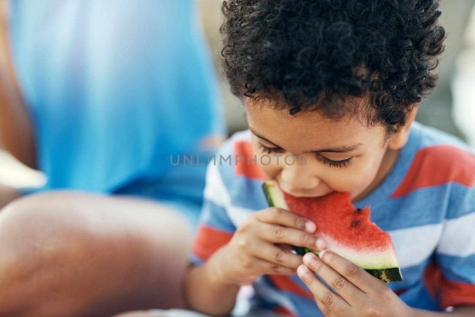 Mom always packs my favourite food. a young boy enjoying a piece of watermelon outside. by YuriArcurs