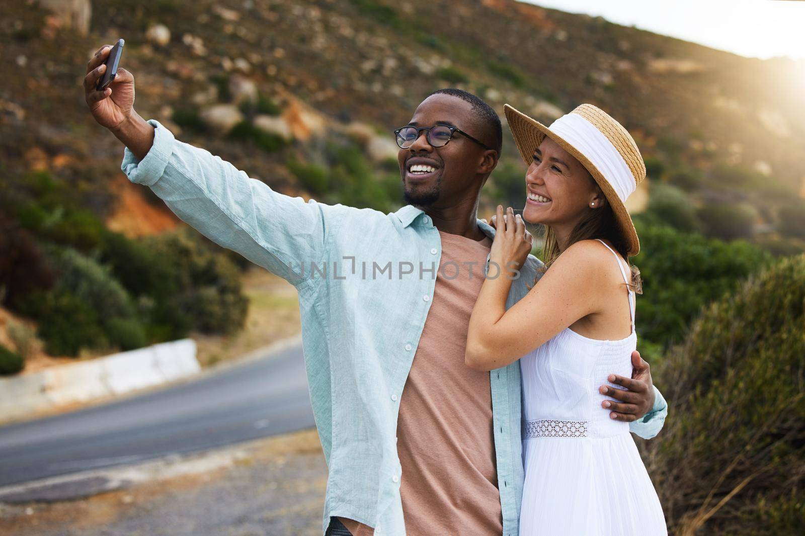 The more we travel the more memories we gain. a happy young couple taking selfies on a road trip. by YuriArcurs