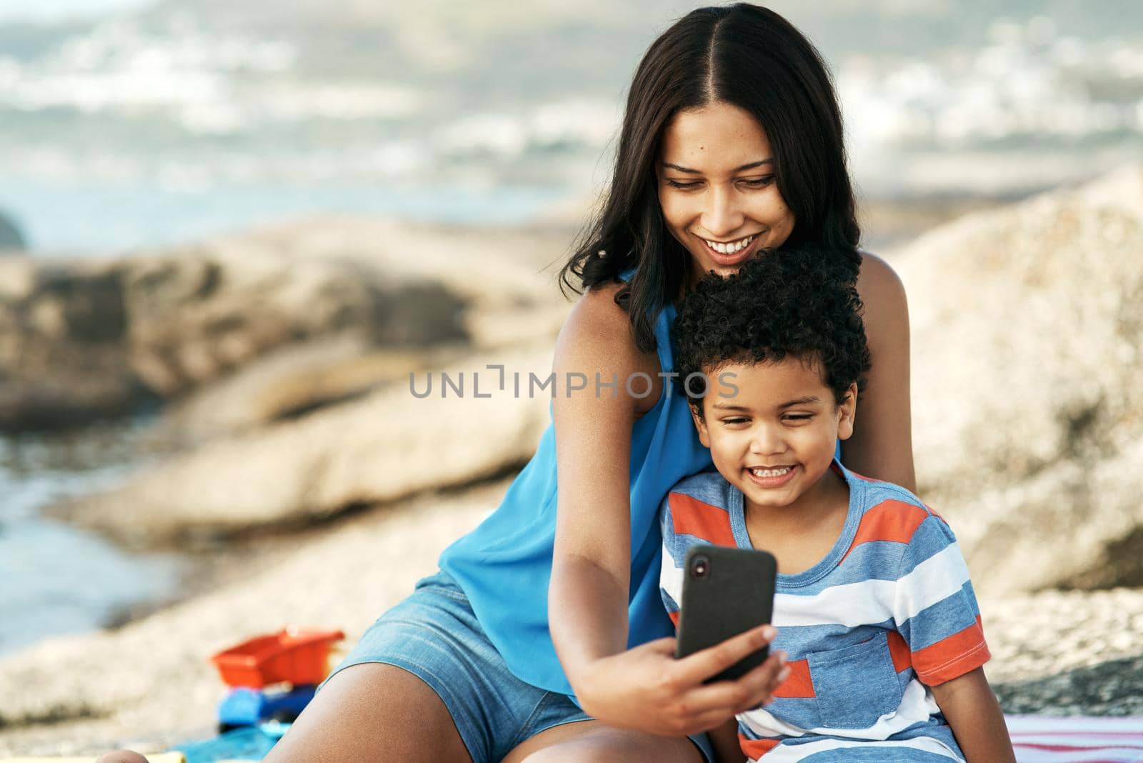 I love spending time with you. a mother and her son taking selfies at the beach. by YuriArcurs