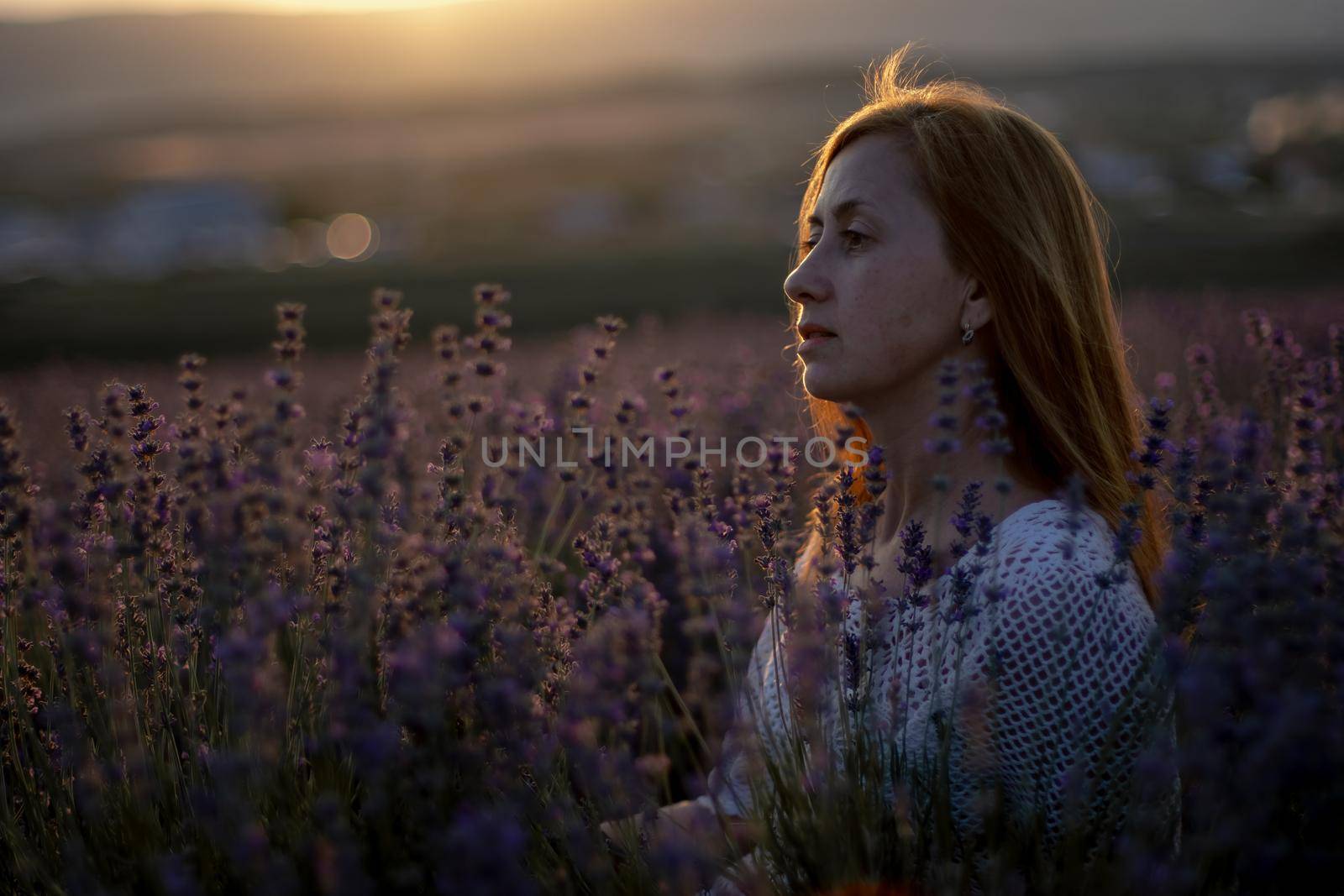 A middle-aged woman sits in a lavender field and enjoys aromatherapy. Aromatherapy concept, lavender oil, photo session in lavender.