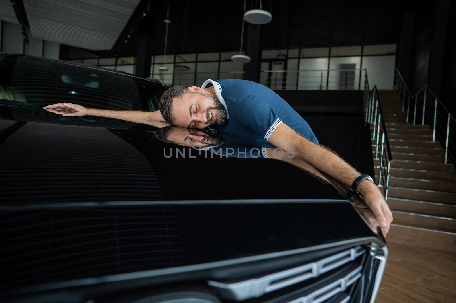 Happy caucasian man hugging the hood of his new car in a car dealership. by mrwed54