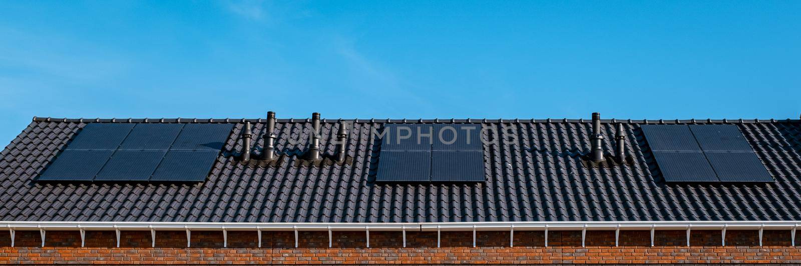 Newly build houses with solar panels attached on the roof against a sunny sky Close up of a new building with black solar panels. Zonnepanelen, Zonne energie, Translation: Solar panel, , Sun Energy.
