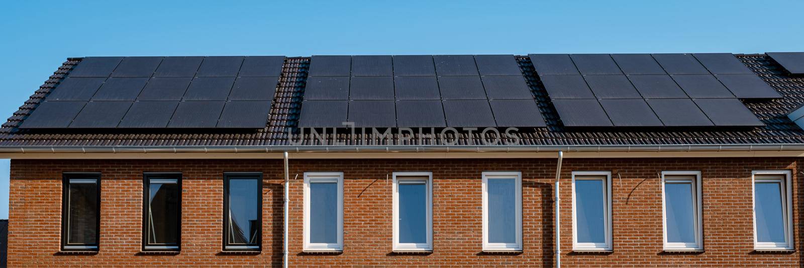 Newly build houses with solar panels attached on the roof against a sunny sky Close up of a new building with black solar panels. Zonnepanelen, Zonne energie, Translation: Solar panel, , Sun Energy.