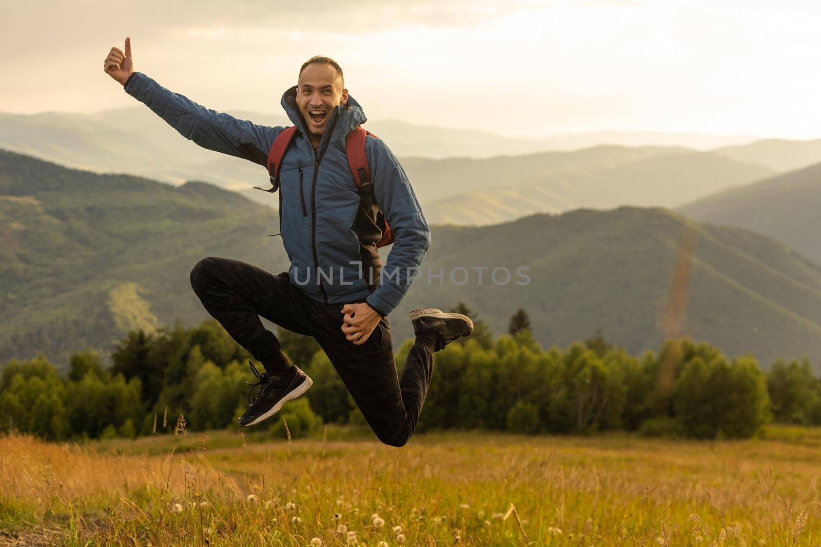 Guy tourist with a backpack stands in the mountains on a meadow with a backpack on his back.