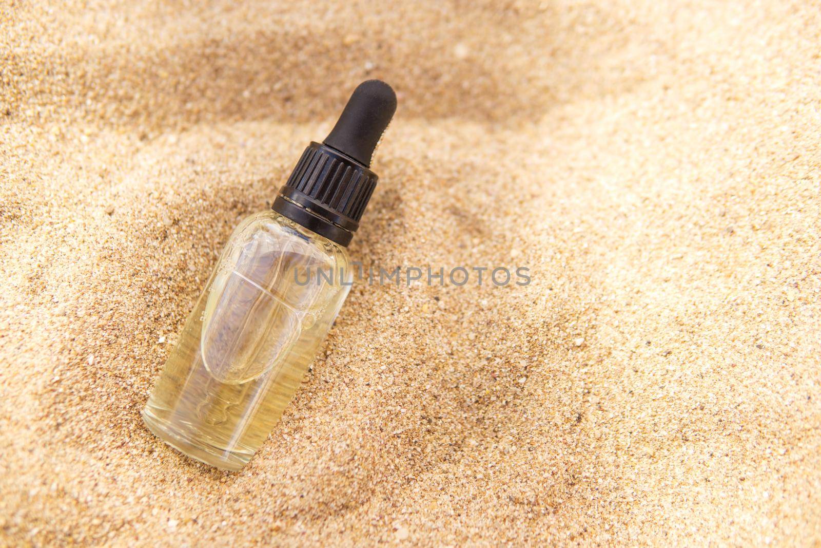 Cosmetic serum for the skin in a glass bottle. A bottle with a pipette on a sandy beach by the sea. Essences for skin care on a sandy background. The concept of natural cosmetics and SPA products.