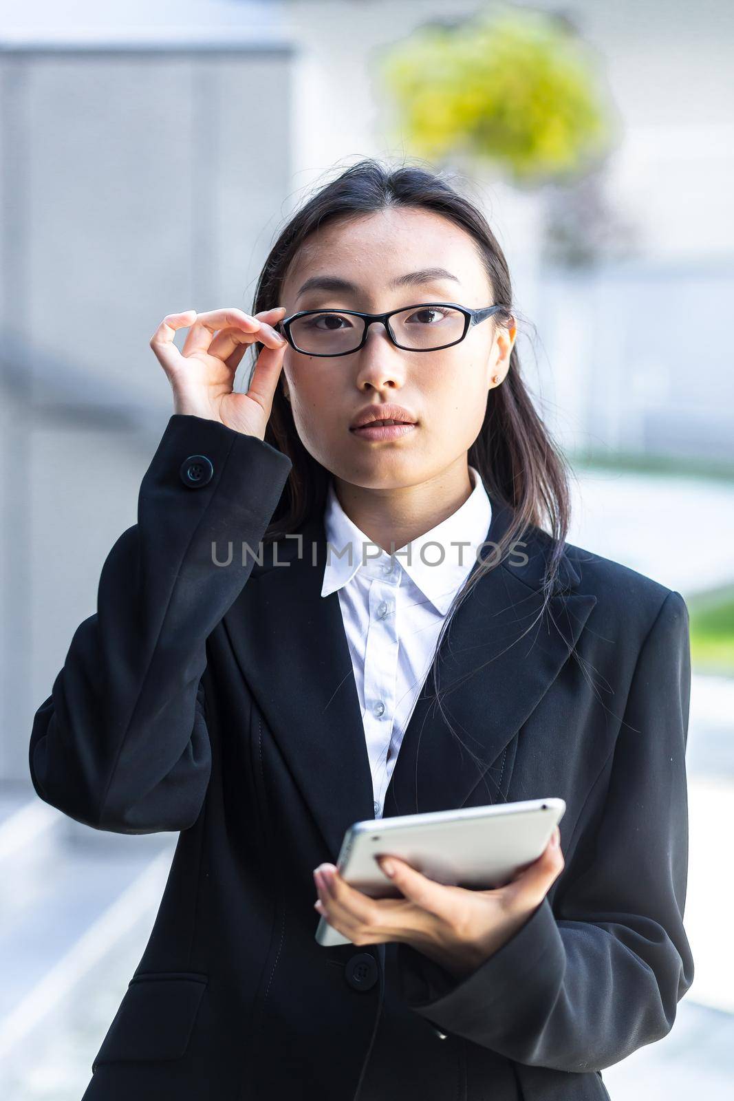 vertical frame, portrait of asian female teacher with glasses looking at camera, and holding tablet computer